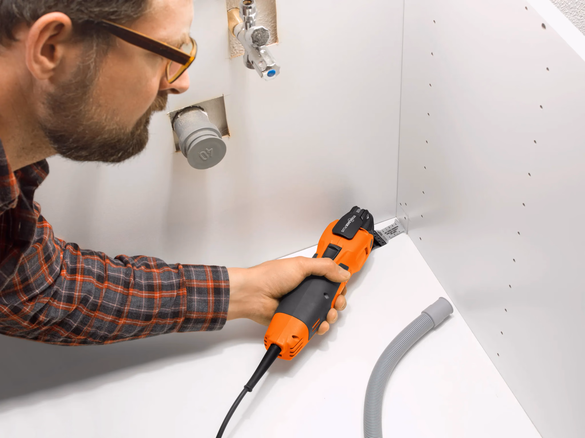Vakman zaagt met een multitool een uitsparing in een witte kastwand